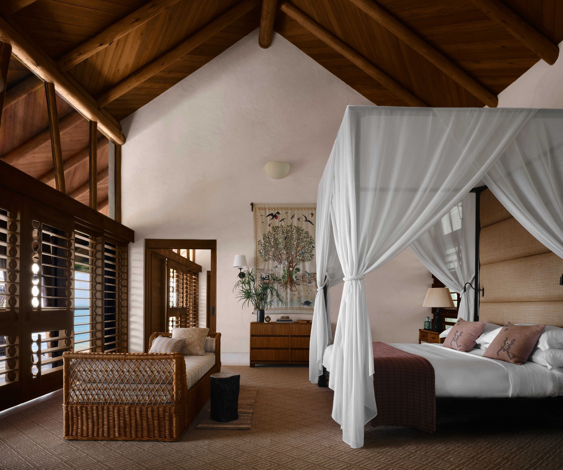 Chambre rustique spacieuse avec un lit à baldaquin, des chaises en osier et des rideaux blancs sous un plafond voûté en bois.