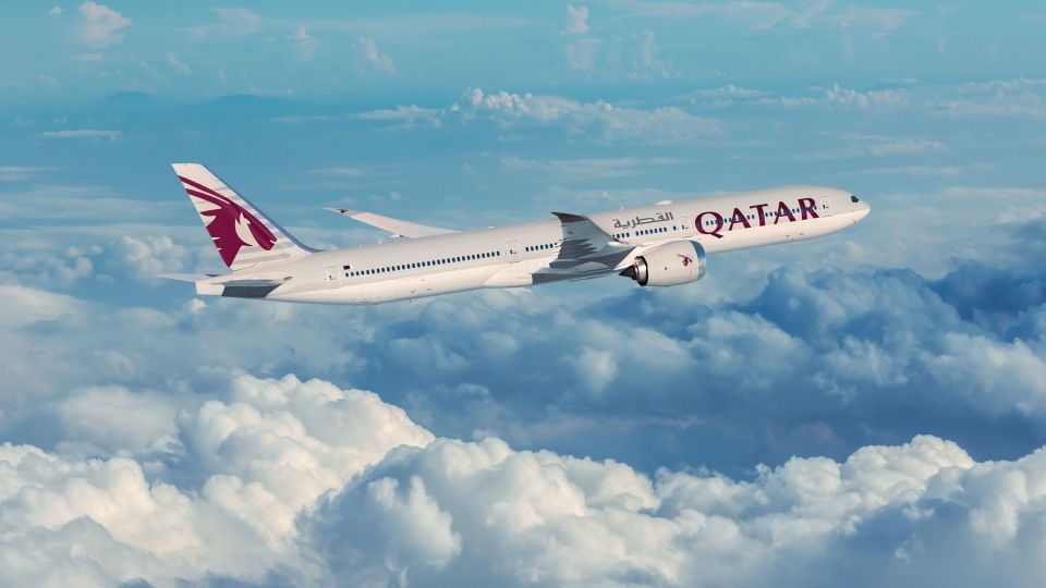 Un avion de Qatar Airways survole les nuages dans un ciel d'un bleu éclatant.