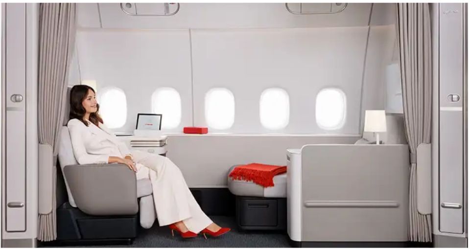 Femme assise dans la cabine d'un avion moderne, utilisant un ordinateur portable près d'un hublot et d'une couverture rouge