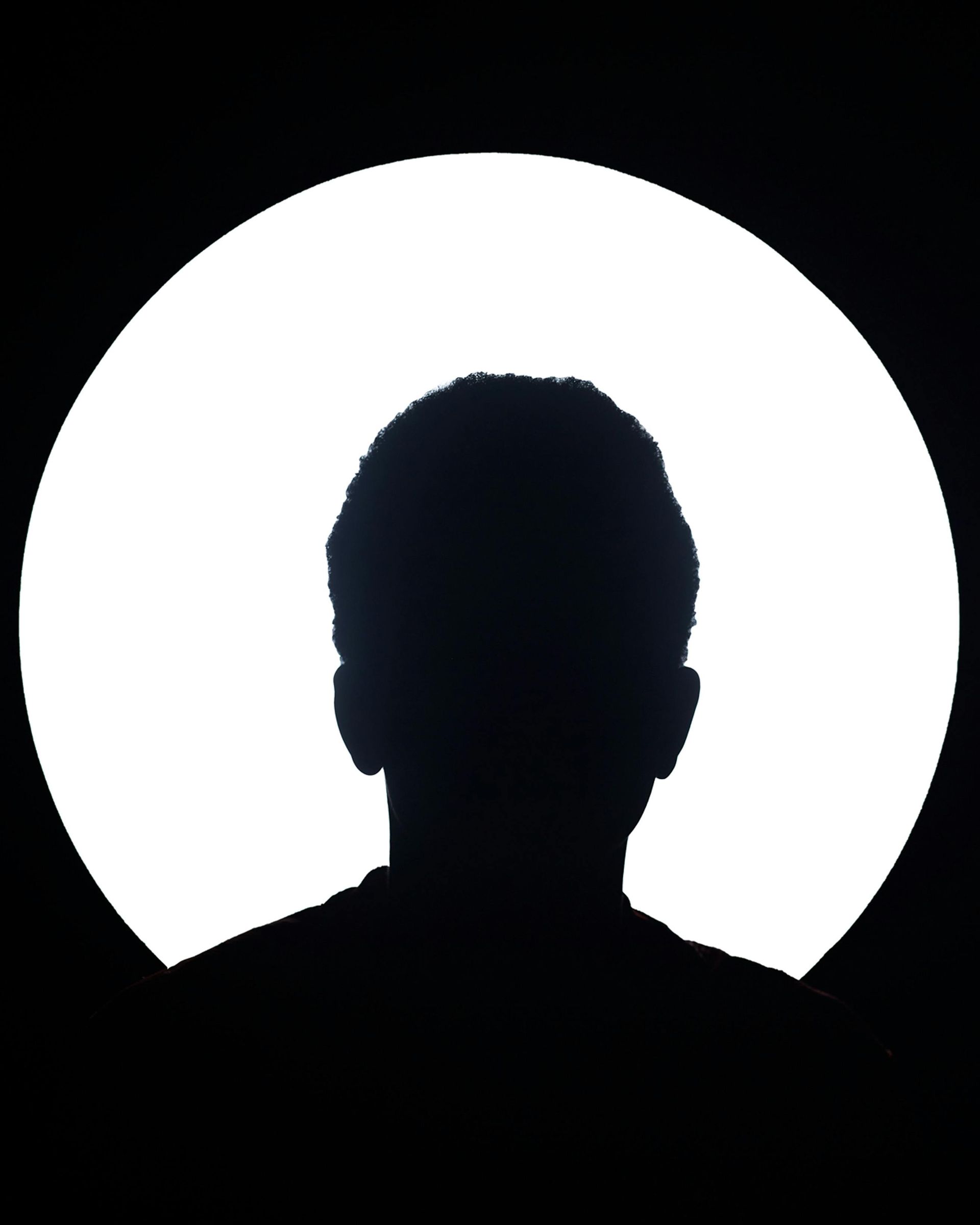 Tête et épaules en silhouette, centrées dans un cercle blanc éclatant sur fond noir.