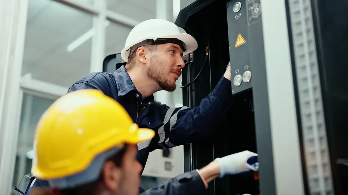 Zwei Männer mit Schutzhelmen arbeiten an einer Maschine.