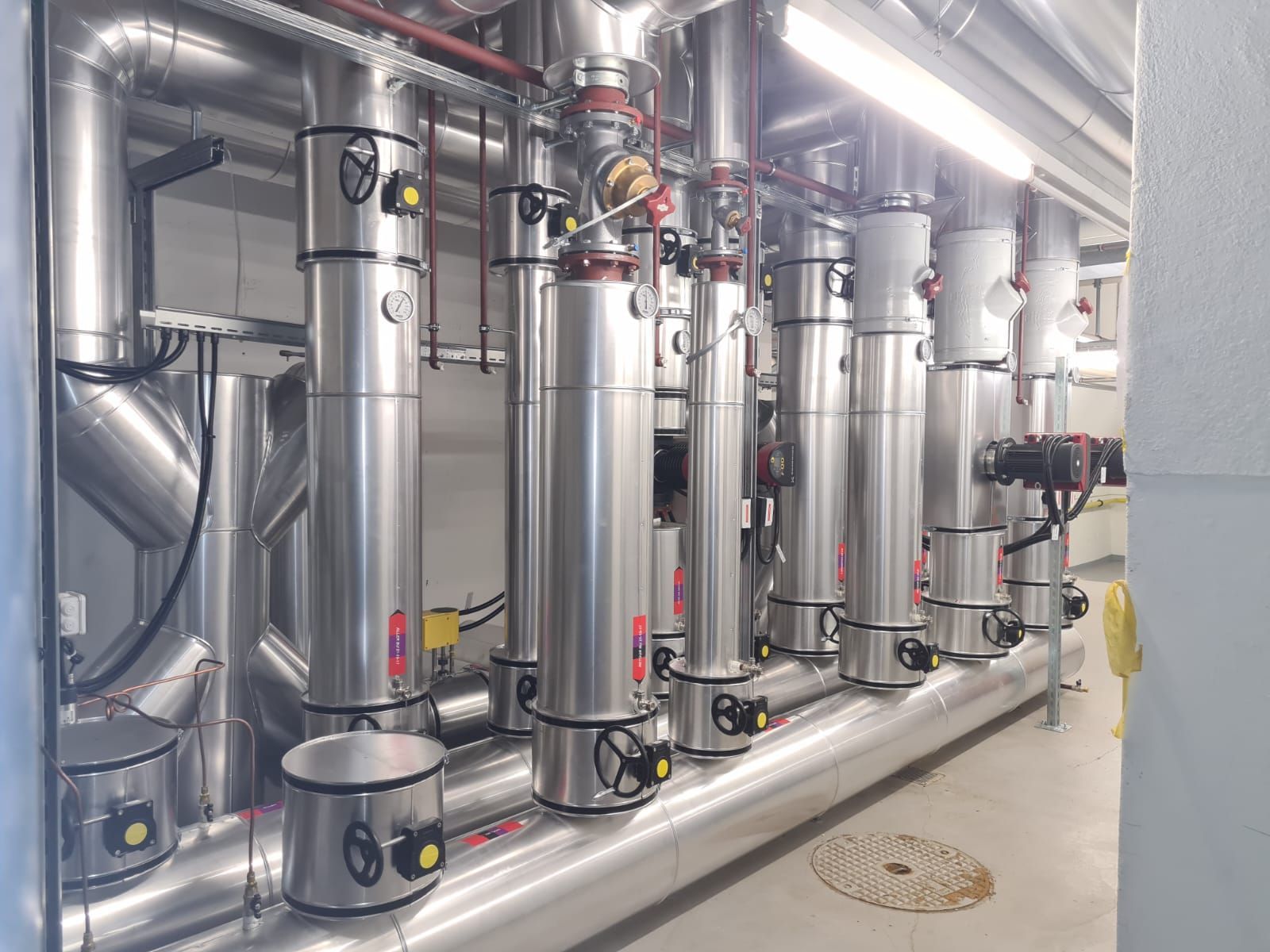 Une rangée de gros tuyaux industriels isolés, équipés de vannes de régulation et de manomètres