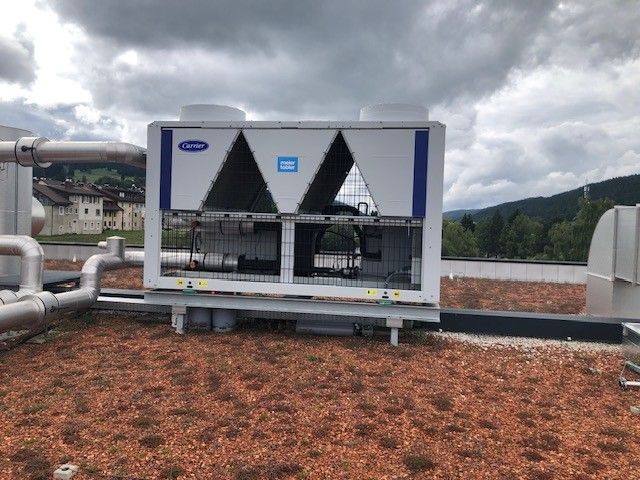 Un groupe frigorifique industriel Carrier installé sur un toit de gravier, avec en arrière-plan des collines nuageuses.