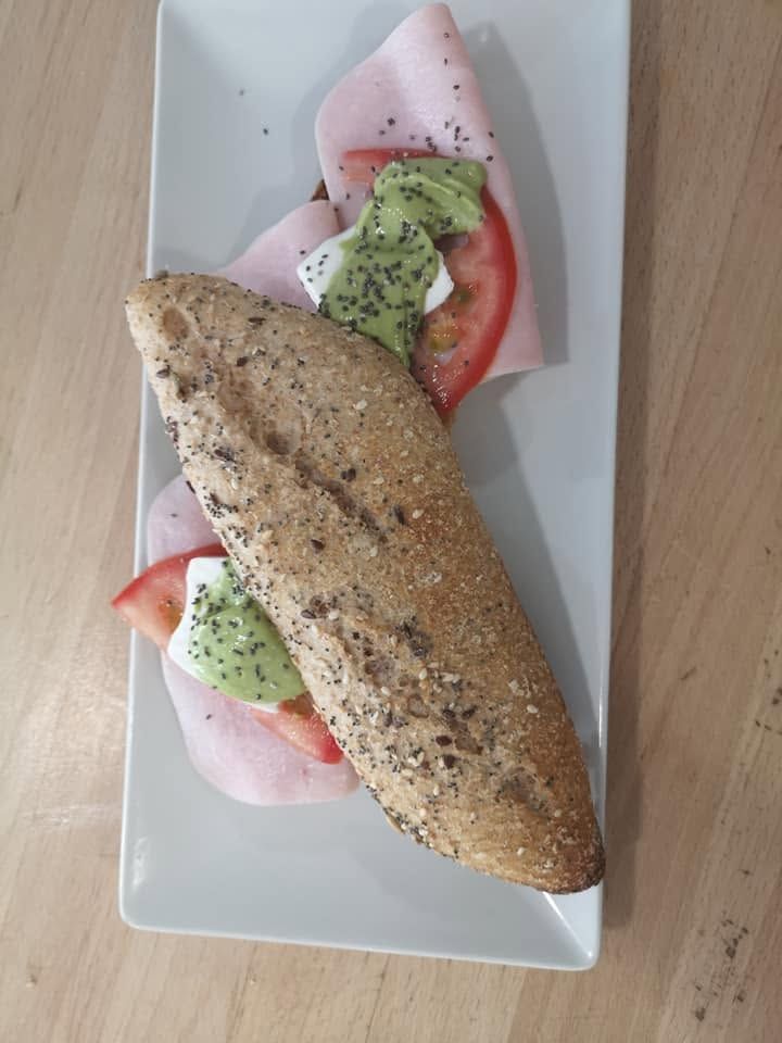 Sándwich abierto con aguacate, tomate y rábano en un plato blanco.