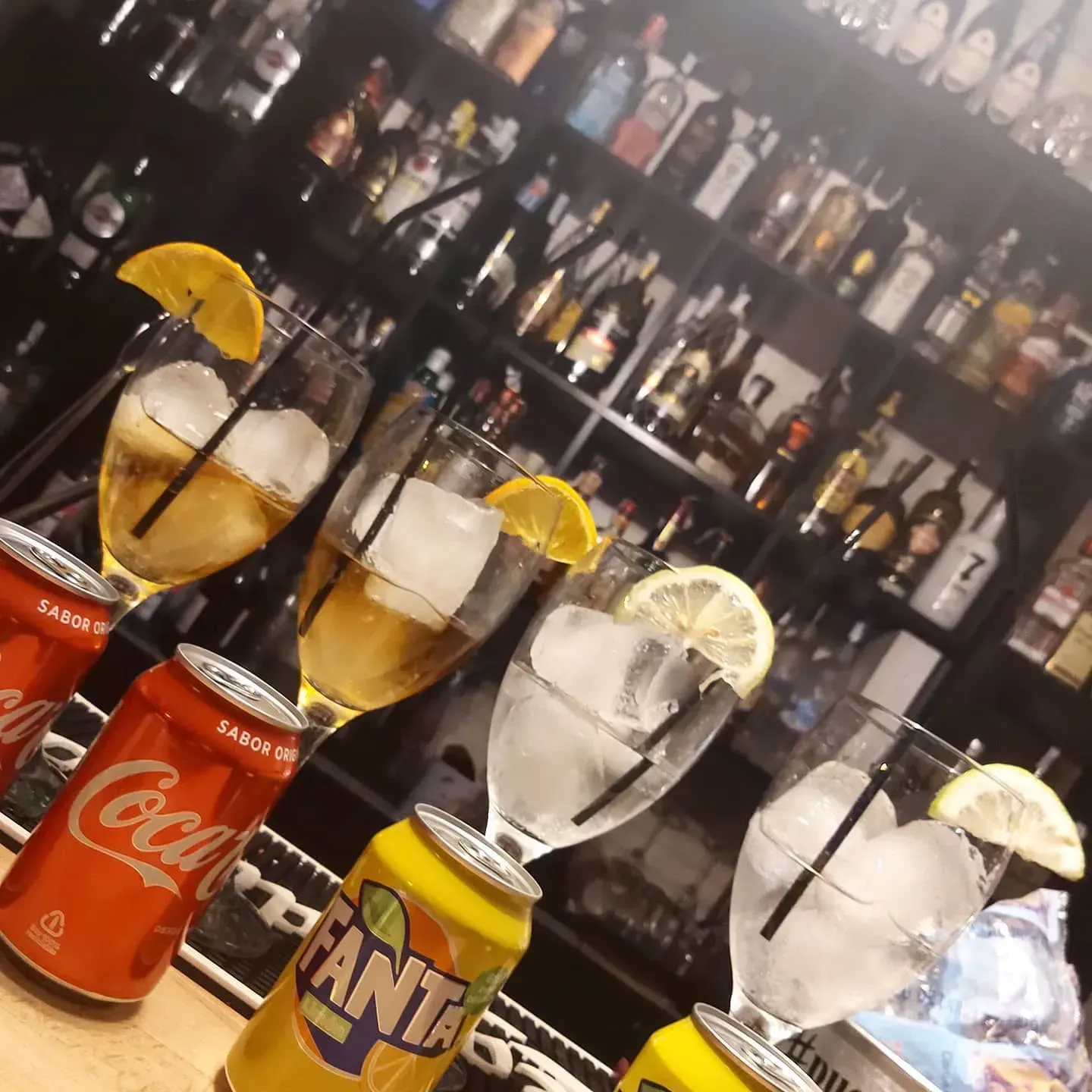 Bebidas con rodajas de limón en la barra, con botellas de licor alineadas en estantes detrás de ellas.