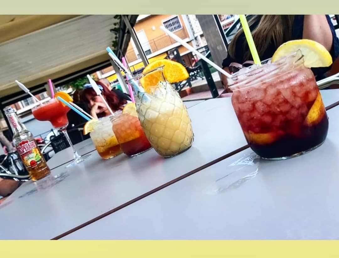 Cócteles con guarnición de cítricos sobre una mesa en un ambiente informal de bar al aire libre.