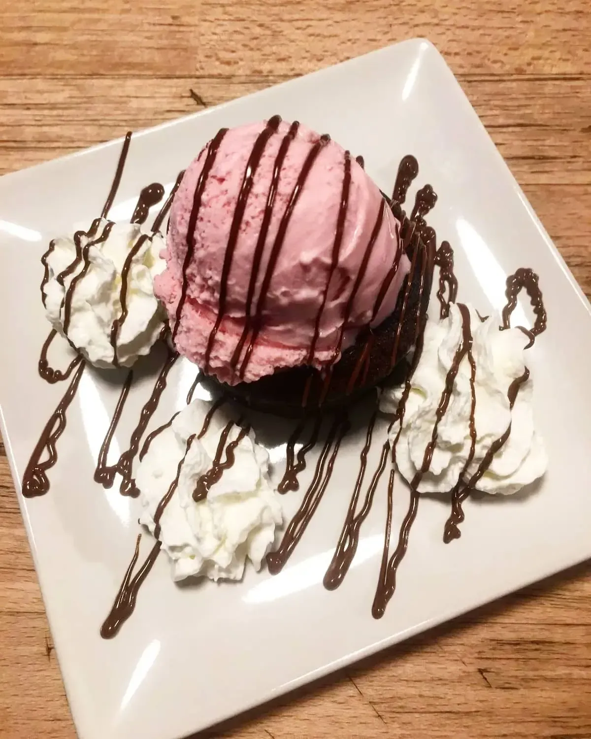 Bola de postre rosa con crema batida y sirope de chocolate sobre un plato blanco.