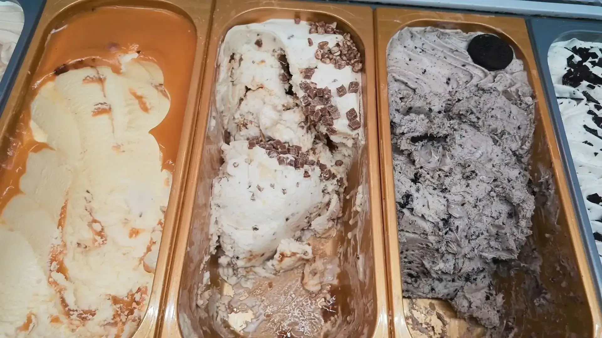 Tres tarrinas vacías de helado con residuos blancos, marrones y grises derretidos en una vitrina refrigerada.