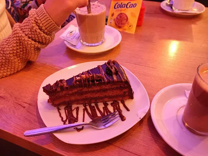 Rebanadas de pastel y café sobre una mesa de madera en una cafetería con iluminación cálida.