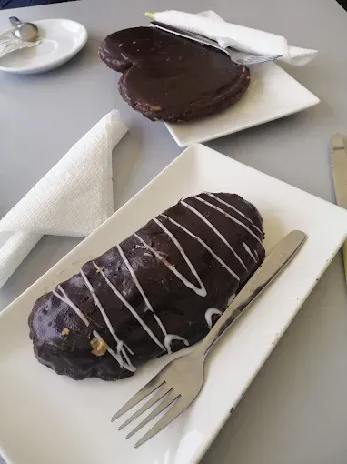 Dos pasteles glaseados con chocolate sobre platos blancos, uno de ellos rociado con glaseado y con un tenedor al lado.