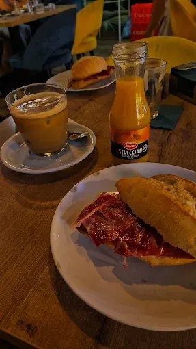 Café y zumo en una mesa de madera con un sándwich y mermelada en una acogedora cafetería.