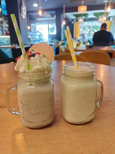 Dos batidos en tarros de cristal con pajitas a rayas y nata montada sobre una mesa de cafetería.