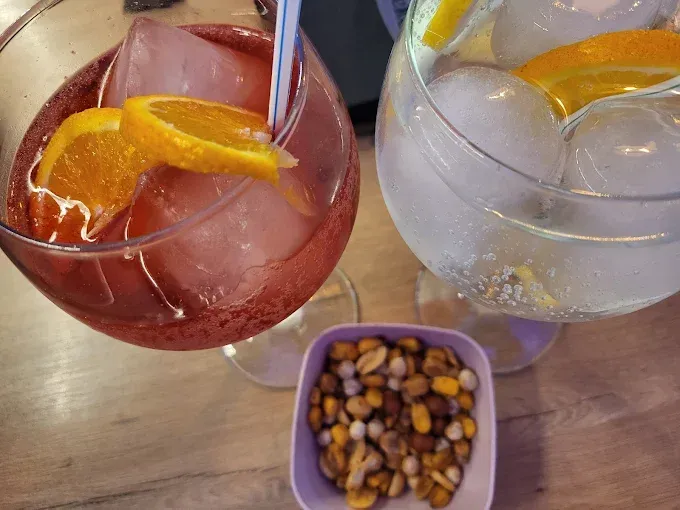 Dos cócteles cítricos sobre una mesa con un cuenco de frutos secos variados.