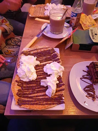 Crepes de postre con crema batida sobre una mesa junto a una bebida y un plato de pasteles.