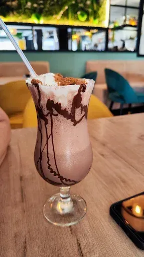 Batido de chocolate en una copa de helado con crema batida y sirope de chocolate sobre una mesa de café.