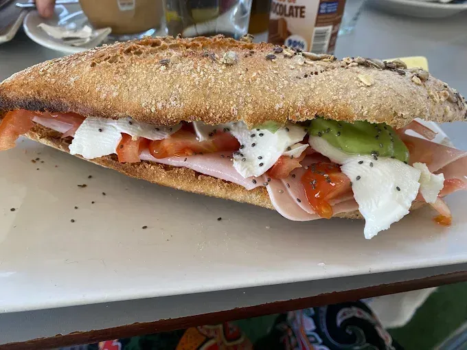 Sándwich grande tipo submarino con tomate, lechuga y queso en un plato blanco.