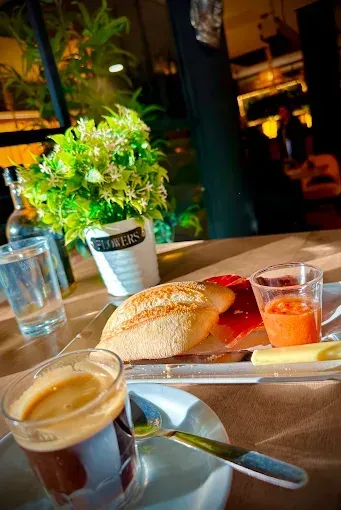 Café y pan en una bandeja en una acogedora mesa de café con una planta en maceta y un vaso de agua.