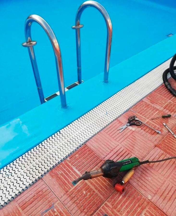 Una piscina con escaleras y una herramienta en el suelo.