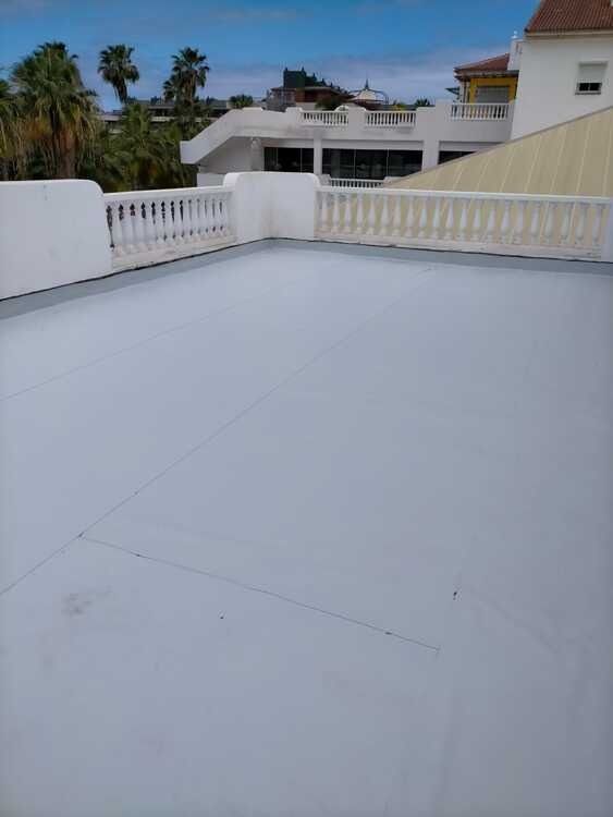 Un techo blanco con un balcón y palmeras al fondo.