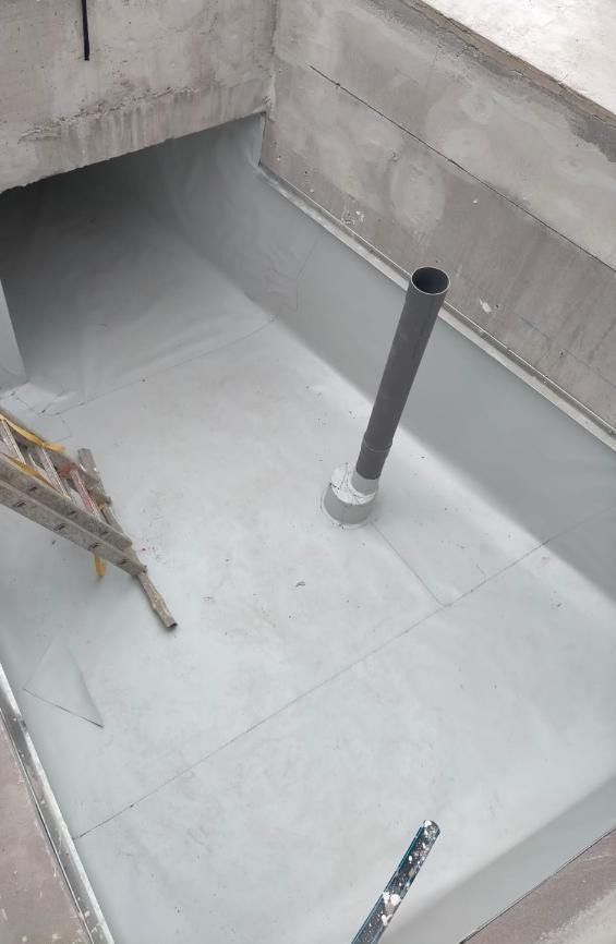 Una escalera está colocada encima de un piso de concreto al lado de una tubería.