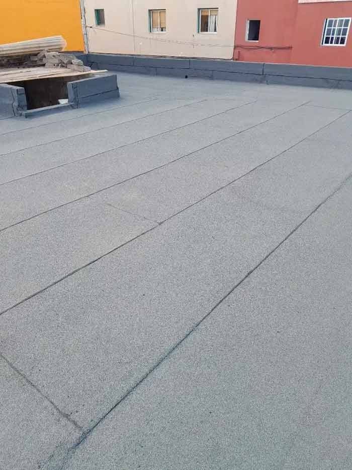 Un tejado con techo gris y un edificio rojo al fondo.