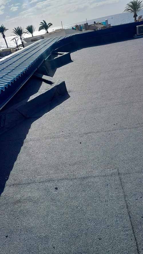 Una superficie de hormigón gris con un techo azul y palmeras al fondo.