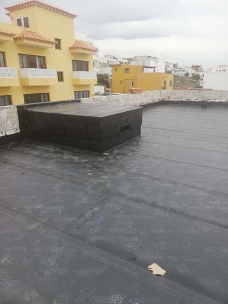Un techo negro con un edificio amarillo al fondo.