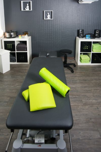 schwarze Massageliege mit grünen Kissen