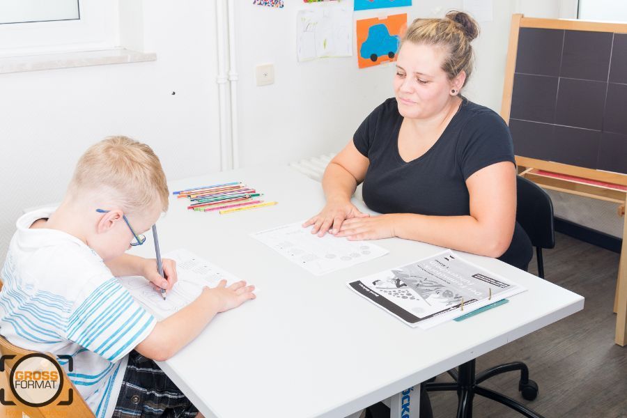 Kind macht Übungen im Zeichnen und Ergotherapeutin beobachtet