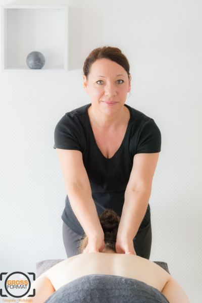 Rückenmassage und die Therapeutin lacht in die Kamera