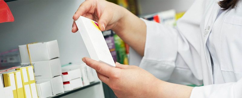 Una farmacéutica sostiene una caja de pastillas en una farmacia.