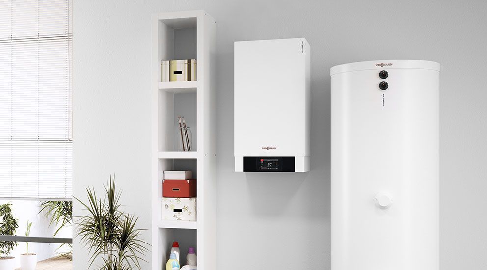 Zwei weiße Heizkessel stehen nebeneinander an einer Wand in einem Wohnzimmer.