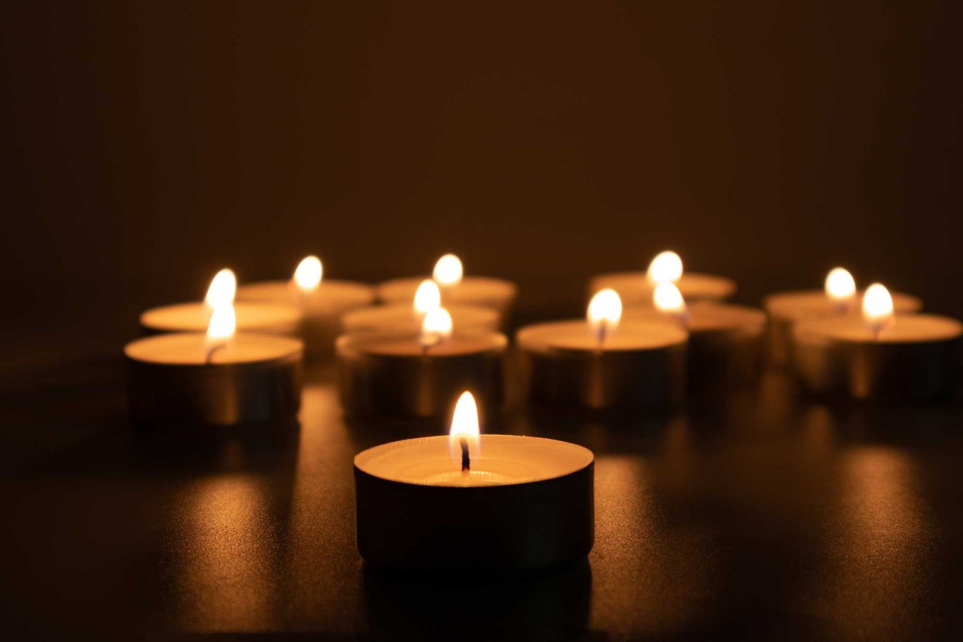 Angezündete Teelichter leuchten auf einer dunklen Oberfläche und erzeugen einen warmen, weichen Bokeh-Hintergrund.