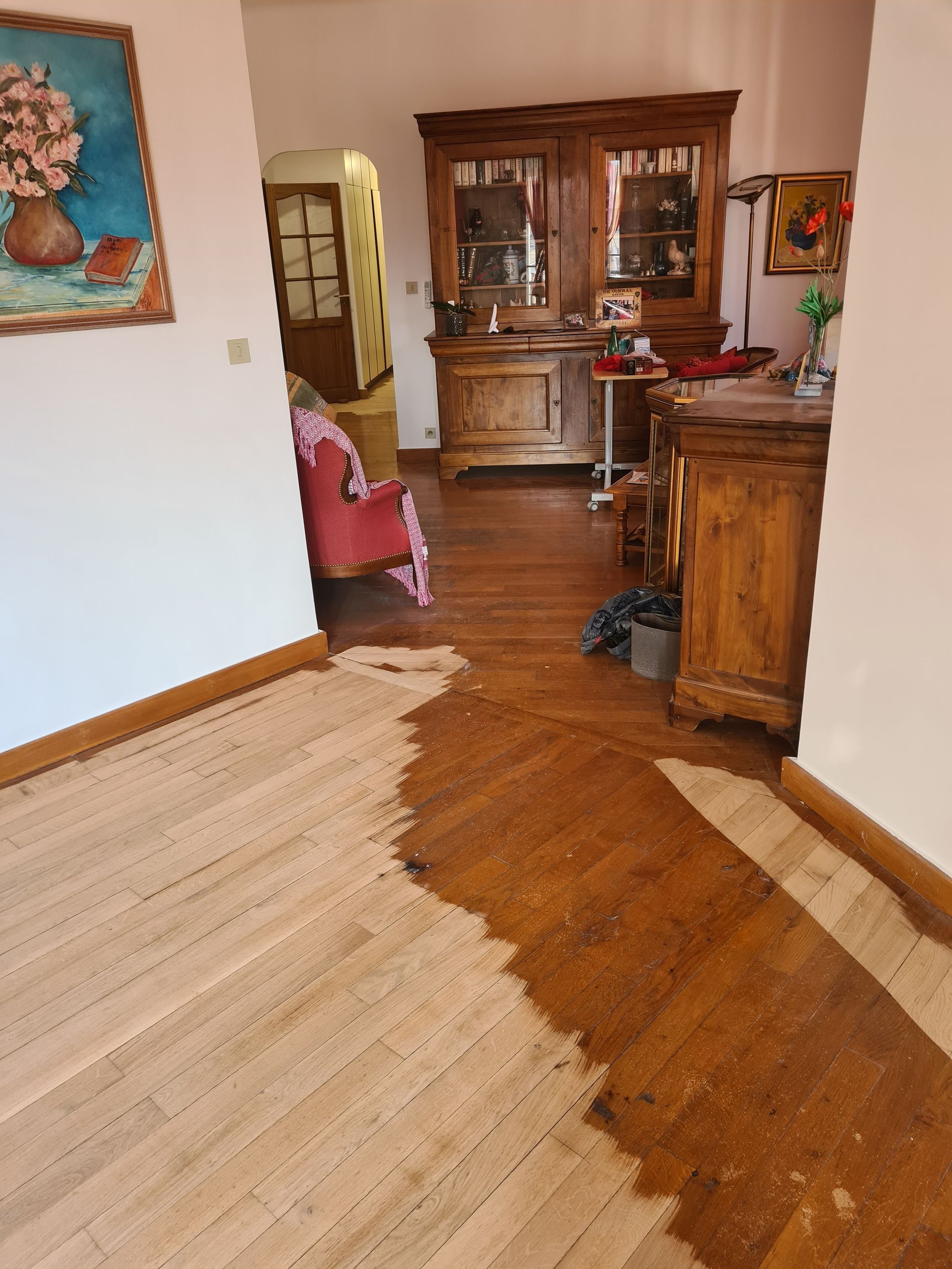 Parquet à la française à moitié poncé dans une pièce avec des commodes et un fauteuil