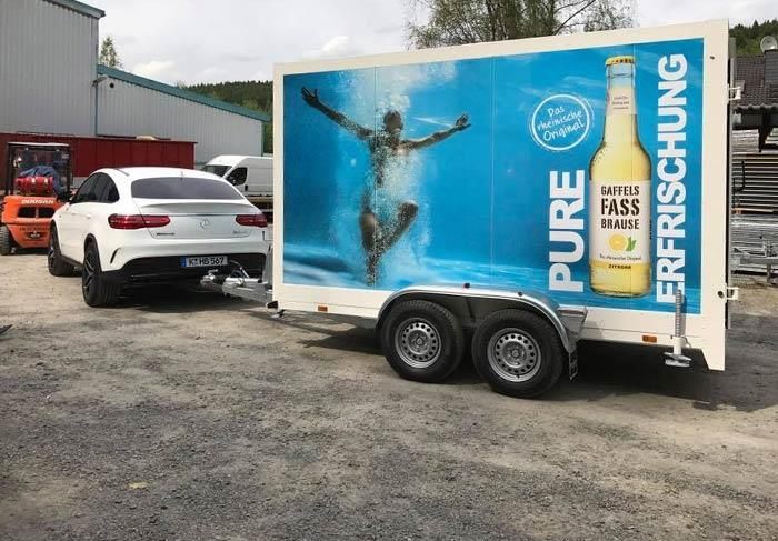 Ein Auto zieht einen Anhänger mit einer Flasche Bier darauf.