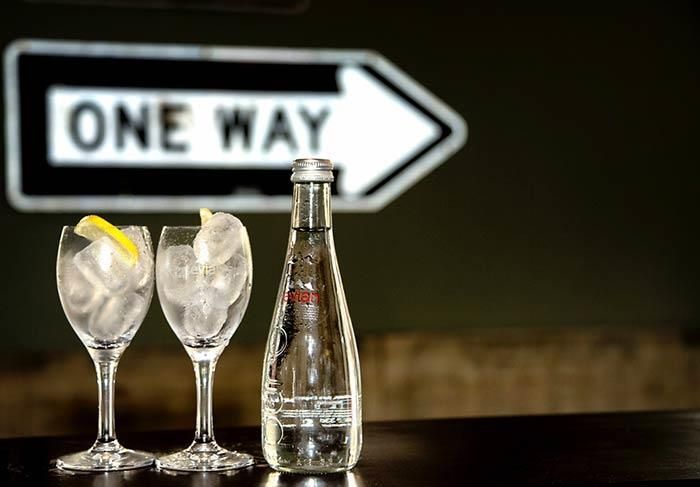Zwei Gläser und eine Flasche Wasser stehen auf einem Tisch vor einem Einbahnstraßenschild