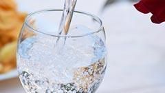 Auf einem Tisch wird ein Glas Wasser in ein Glas gegossen.