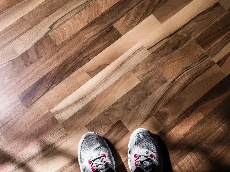 Zapatillas deportivas sobre un suelo de madera iluminado por el sol, con luz y sombra diagonales.