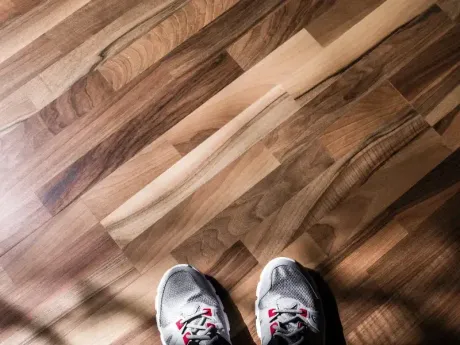 Zapatillas deportivas sobre un suelo de madera iluminado por el sol con sombras diagonales.
