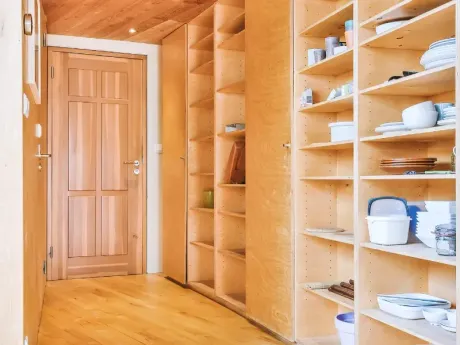 Despensa de madera con estantes empotrados llenos de vajilla y una puerta cerrada al final de un pasillo.