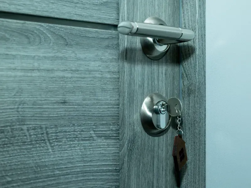 Primer plano de una puerta de madera con manija plateada y llave en la cerradura.