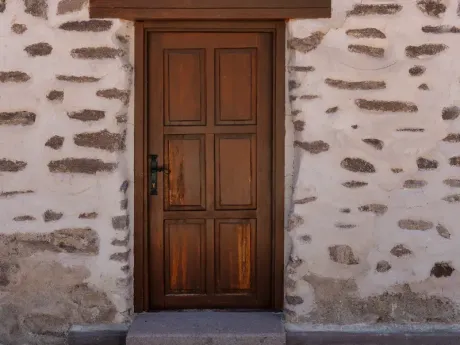 Puerta de madera enmarcada en una pared de piedra blanca con un pequeño escalón en la entrada.