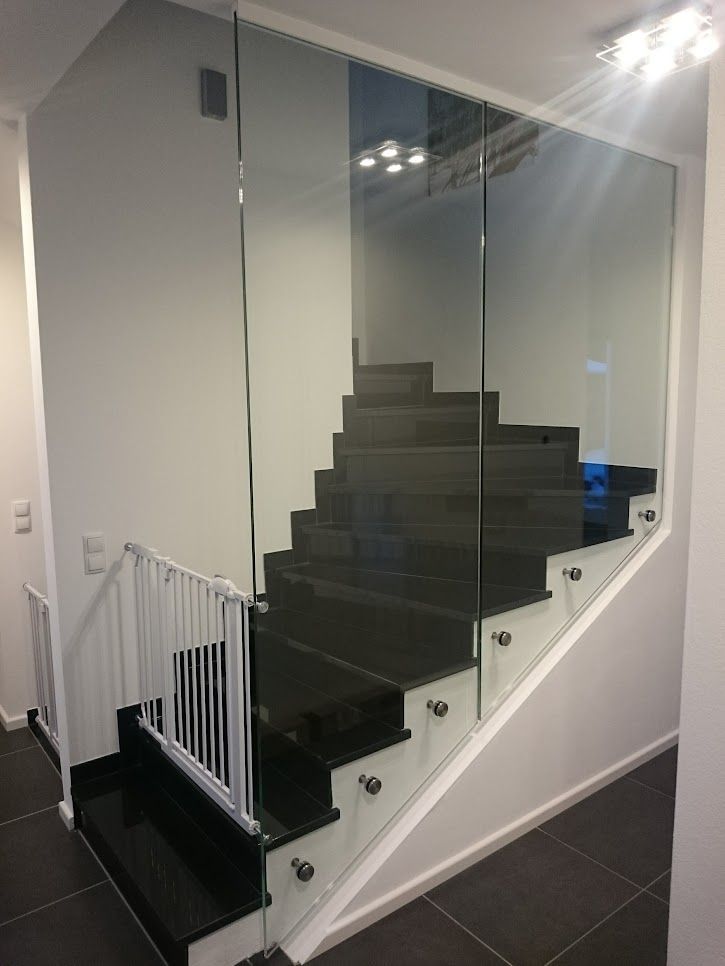 Treppe mit dunkelgrauen Stufen und Seitenteilen aus Glas. Unten befindet sich ein weißes Treppengitter.