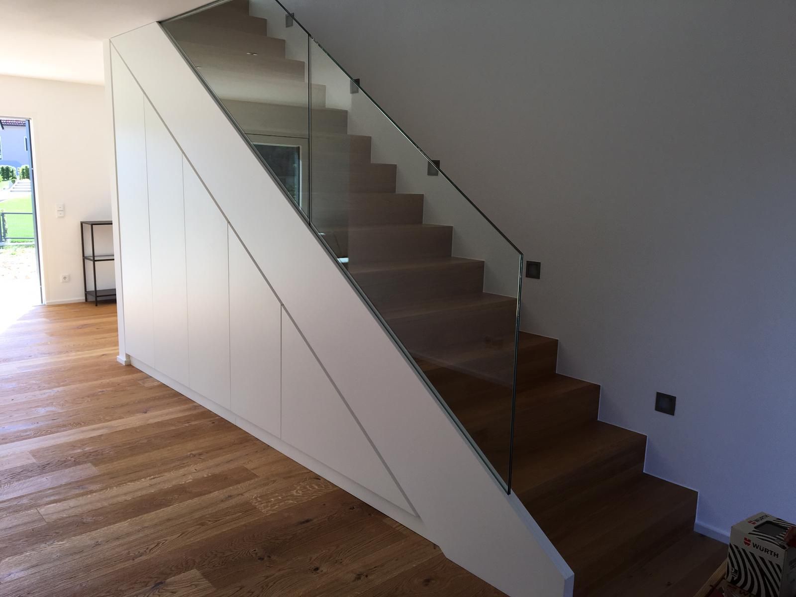Moderne Treppe mit Holzstufen, Glasgeländer und weißer Verkleidung.