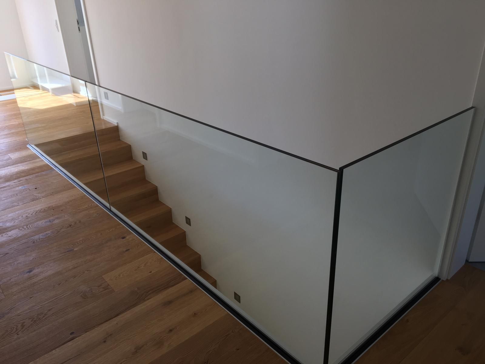 Glasgeländer neben einer Holztreppe in einem hellen, modernen Haus.
