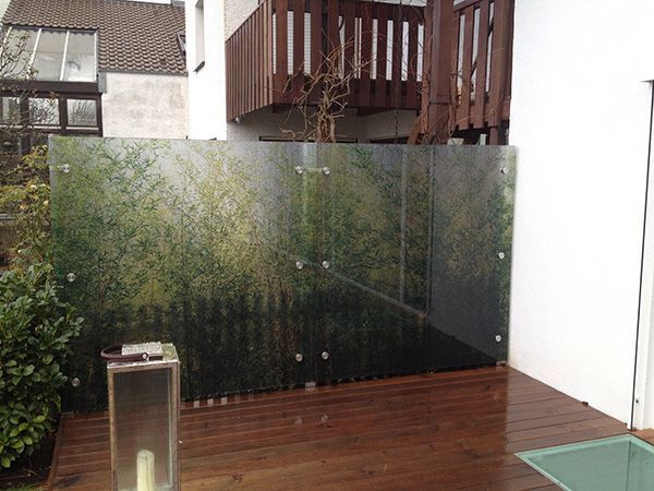 Außenglasplatten mit Waldszenenaufdruck, die ein Holzdeck von einem Gebäude trennen.