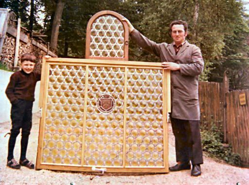 Ein Mann und ein Junge halten im Freien ein großes, verziertes Fenster mit Wabenglas.