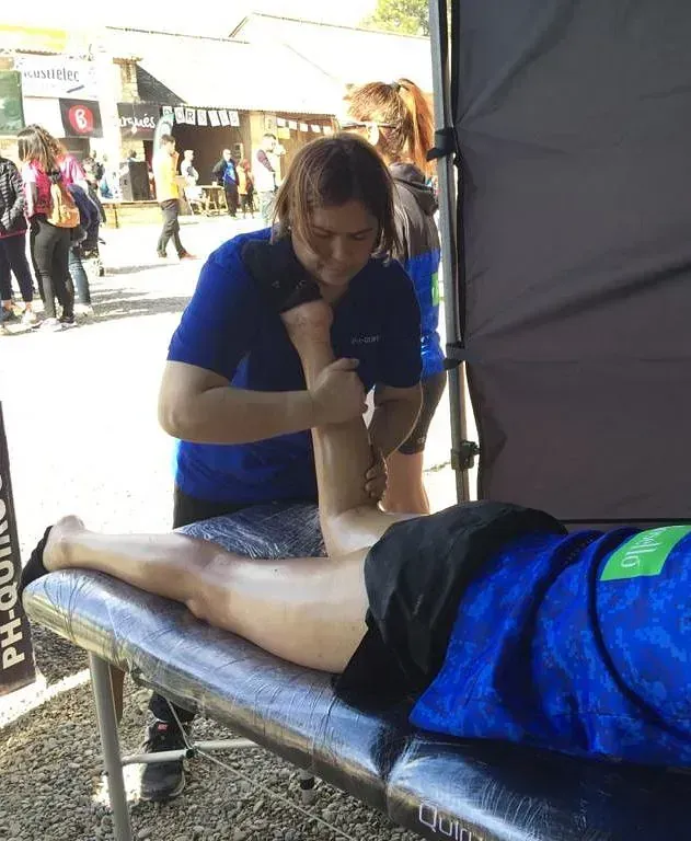 Una mujer con una camisa azul está masajeando la pierna de una persona.