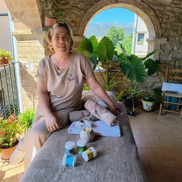 Una mujer está sentada en una mesa de masajes con plantas en el fondo.