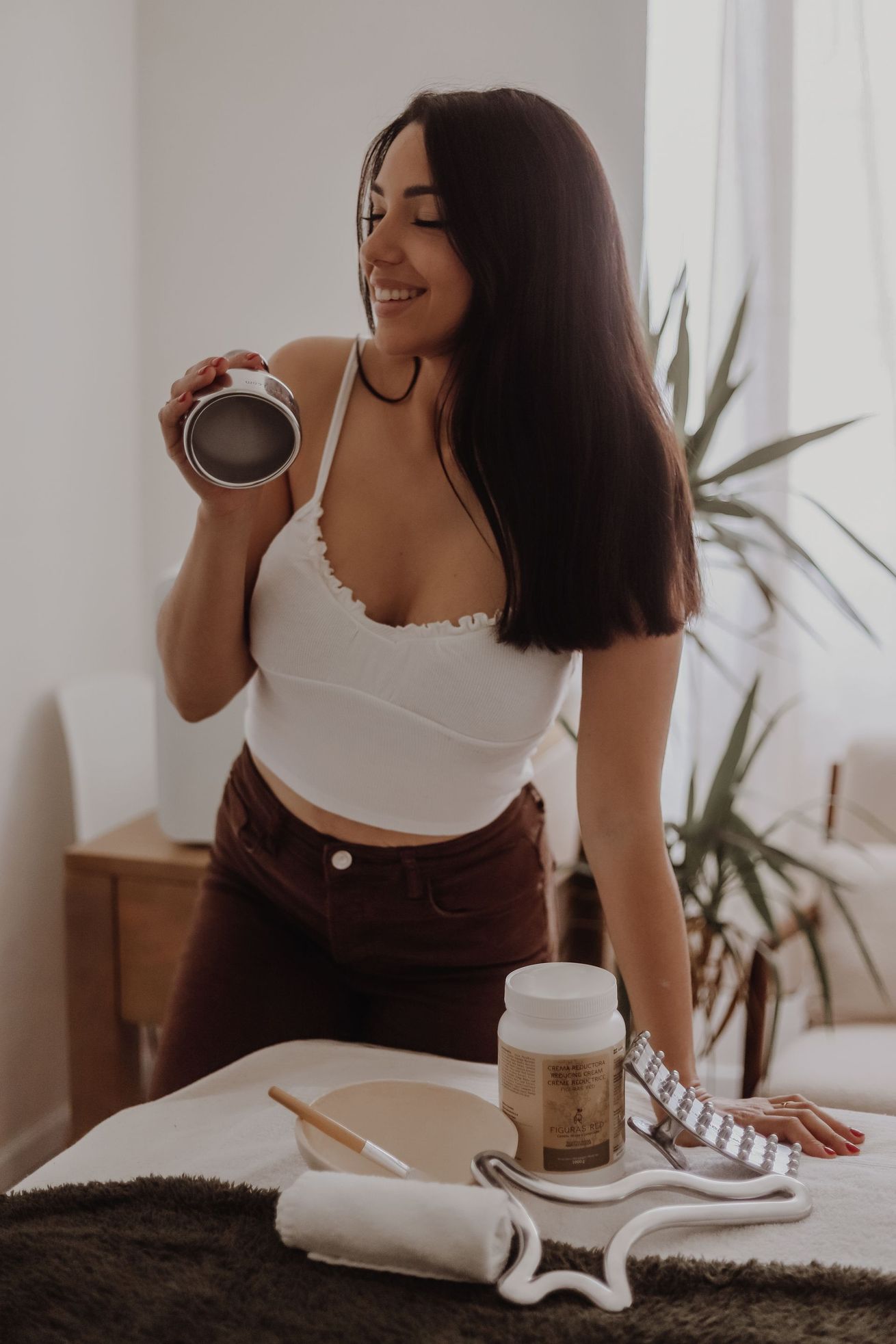 Femme tenant un pot à côté d'un meuble-lavabo contenant des produits de soins capillaires et cutanés.